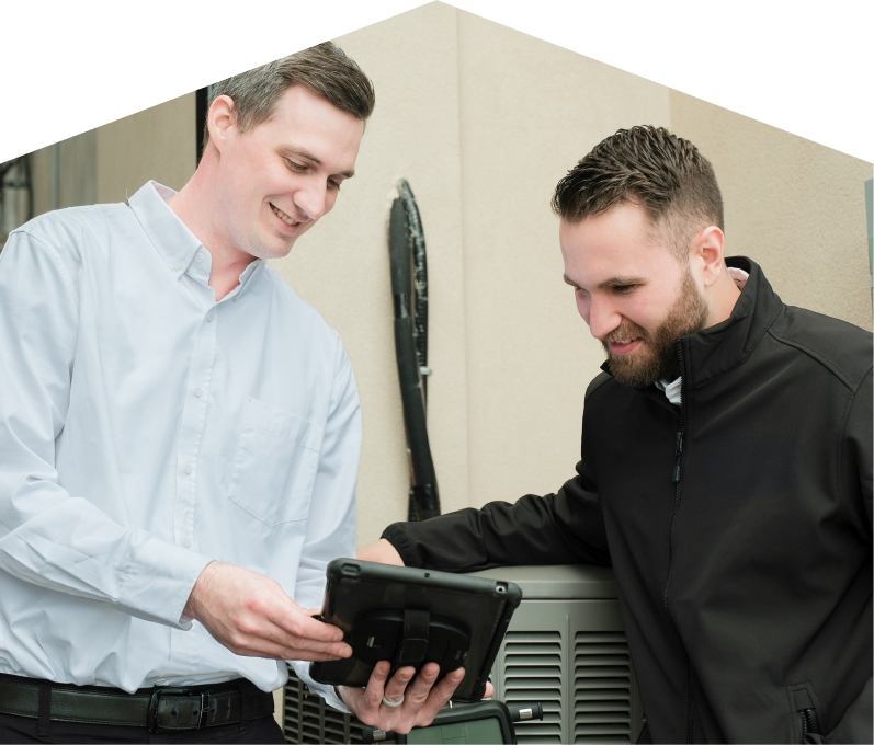 A Mersey technician in a white shirt shows service details on a tablet to a smiling client in a black jacket, standing beside an AC unit outside a beige building.
