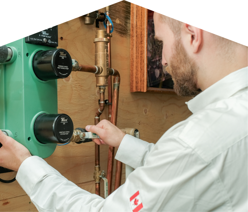 Mersey HVAC specialist performing boiler installation, securing a valve on a new hydronic heating system with copper piping and a green circulation pump mounted on a wooden wall.
