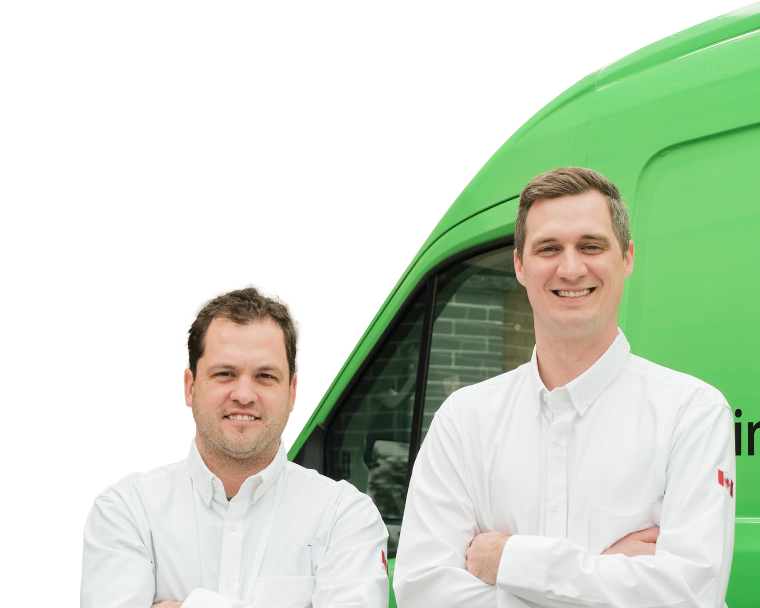 Two Mersey technicians smiling in front of their green service van, wearing issued jackets during an on-site consultation.