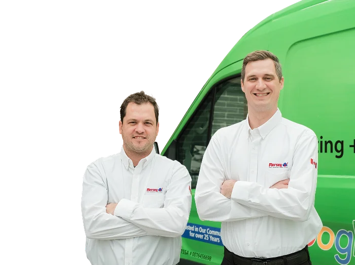 Two Mersey technicians smiling in front of their green service van, wearing issued jackets during an on-site consultation.